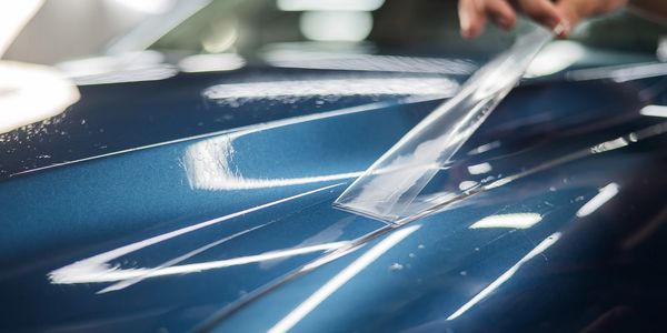 Hand applying protective film on shiny blue car surface.