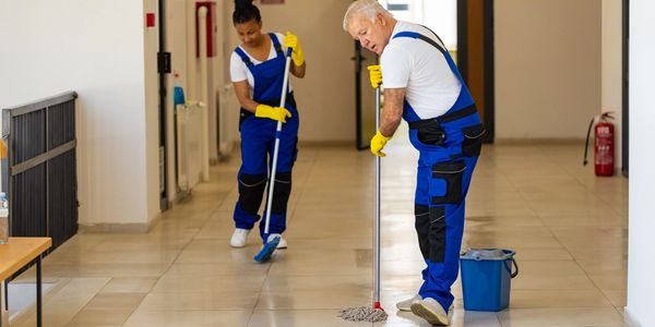Two janitors cleaning a hallway with mops and gloves.
