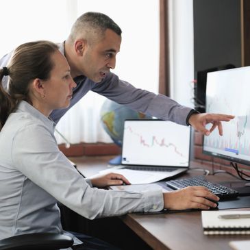 Two professionals analyzing financial charts on computer screens in an office.