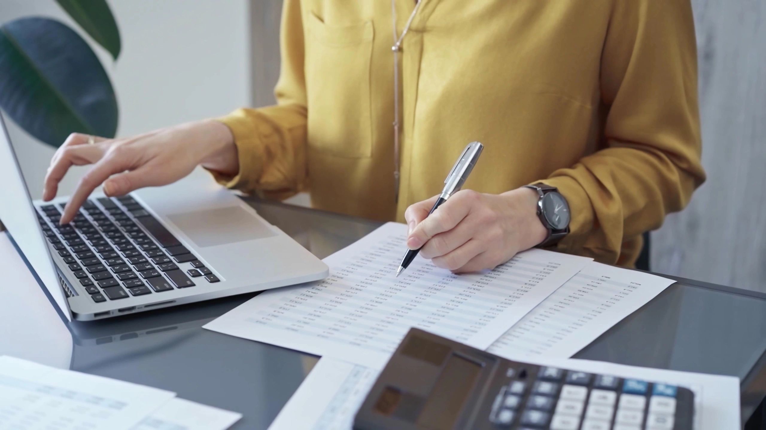 Person working with financial documents and a laptop at a desk.