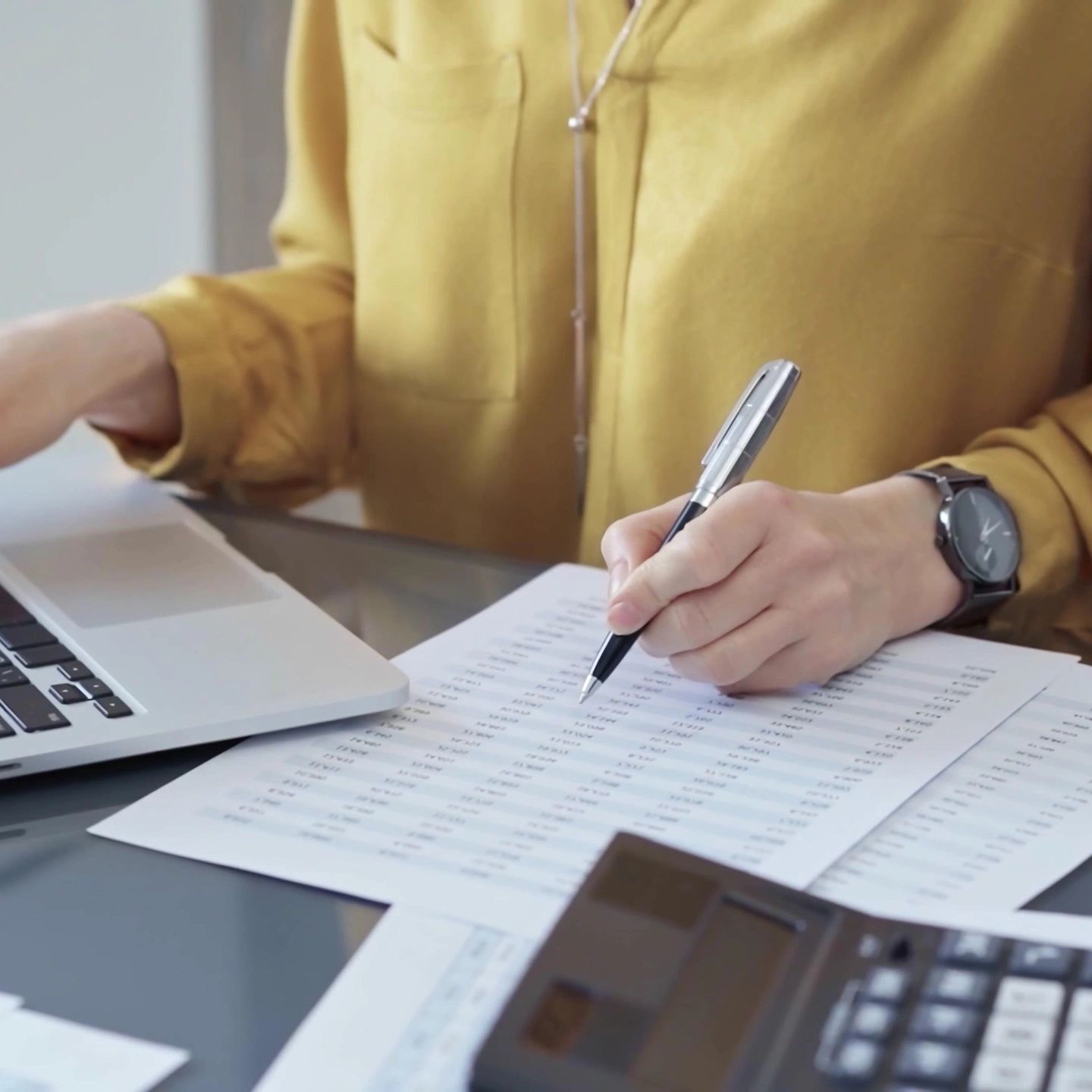 Person working with financial documents and a laptop at a desk.
