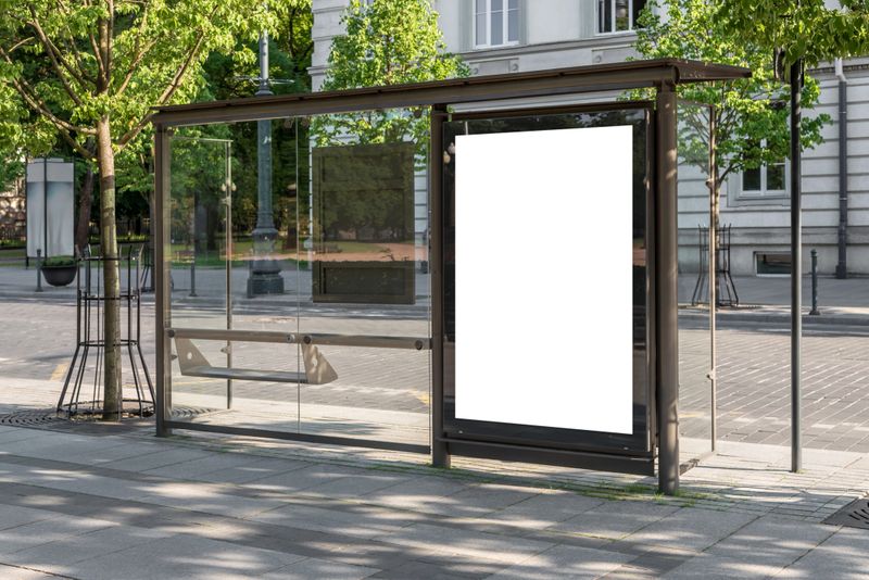 Blank White Bus Stop Vertical Billboard Mockup In Front Of An Empty Street. Outdoor Advertising Lightbox On The Sidewalk