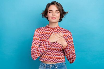 une femme les yeux fermés, un sourire aux lèvres et deux mains sur son coeur signe d'auto-compassion