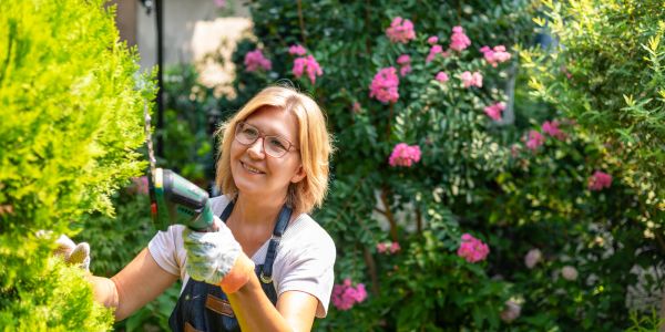 Woman gardening with a power tool in a flower garden.