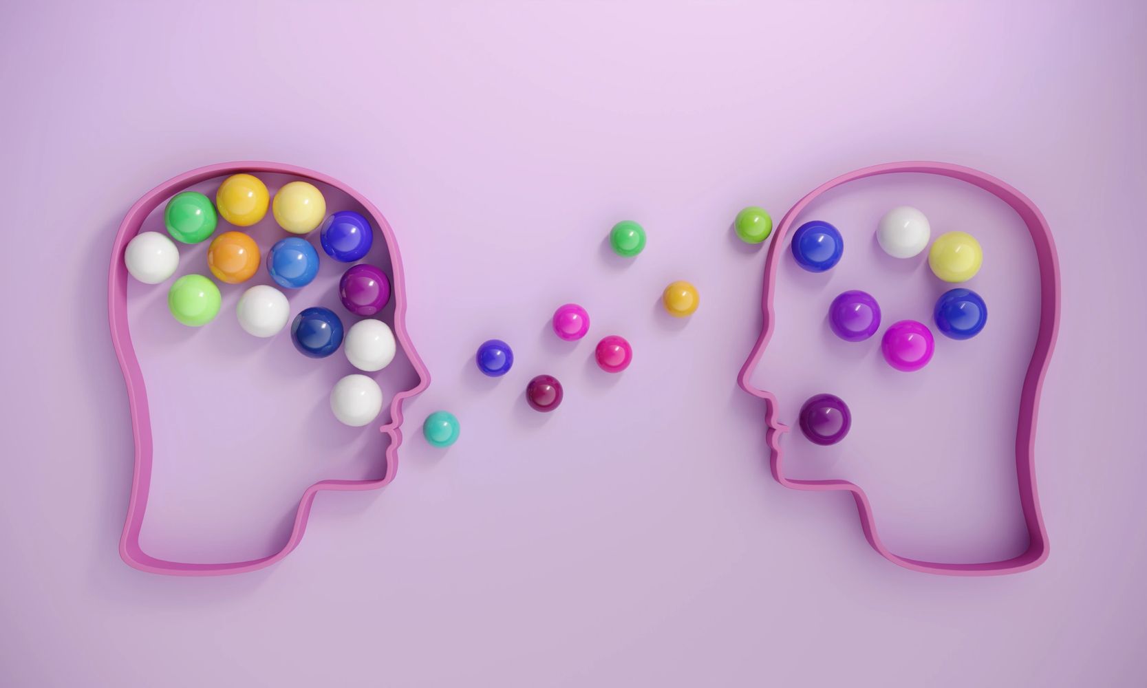 Two head outlines exchanging colorful spheres, symbolizing communication and idea sharing.