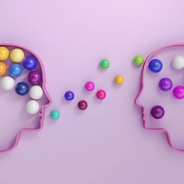 Two head outlines exchanging colorful spheres symbolizing ideas or knowledge transfer.
