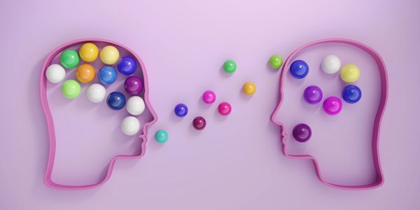 Two head outlines exchanging colorful spheres, symbolizing communication and idea sharing.