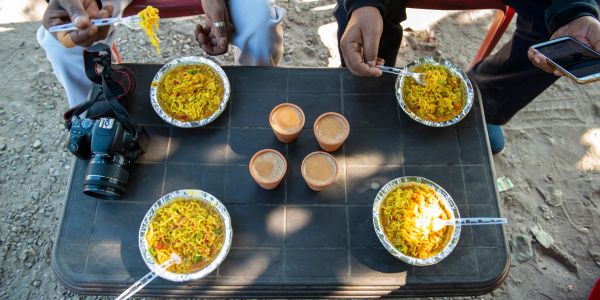 Four people eating noodles with drinks on a table outdoors.