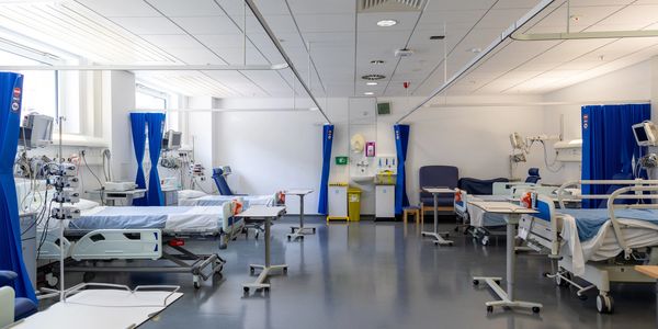 A clean, empty hospital ward with multiple beds and medical equipment.