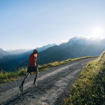 Runner jogging uphill on a mountain trail during sunrise.