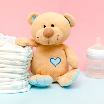 Baby essentials with diapers, a teddy bear, and a feeding bottle on pastel background.