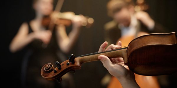 Close-up of violin playing with blurred musicians in the background.