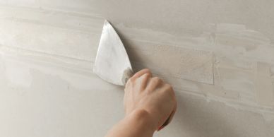Hand scraping wall surface with a putty knife.