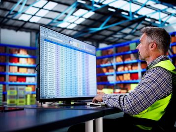 Warehouse worker analyzing data on a large computer screen.