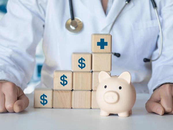 A doctor is standing behind a stack of blocks with money on top.
