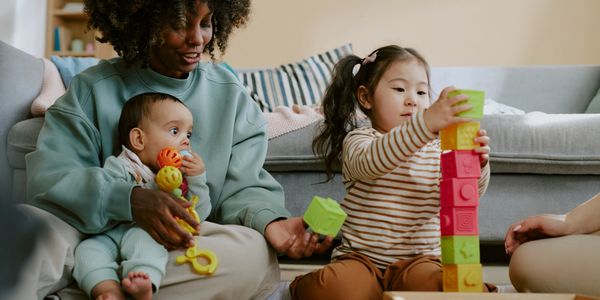 A woman and two children play with colorful blocks on the floor.