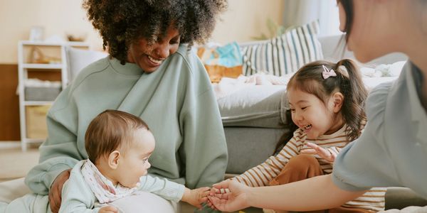 Two women and two children smiling and holding hands indoors.