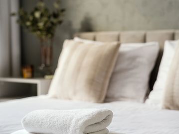 Neatly folded white towels on a bed with beige pillows.