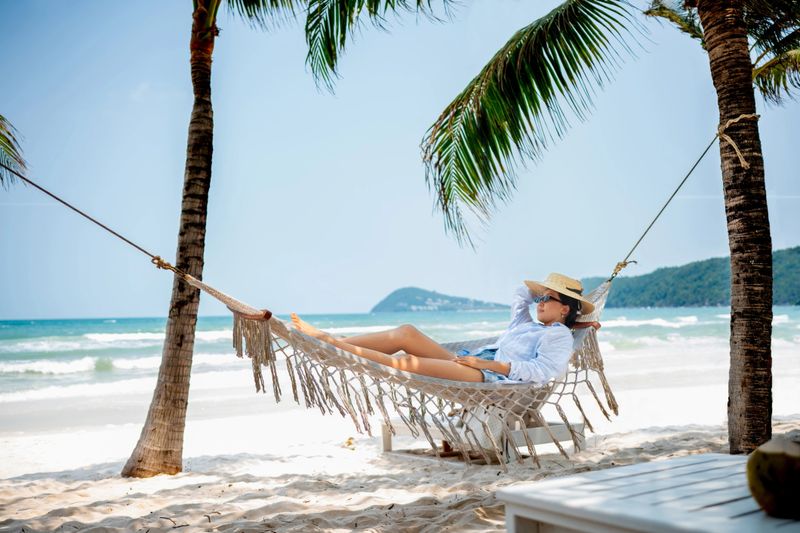 Asian traveler relaxing at the beach on a hammock and enjoying her summer vacations