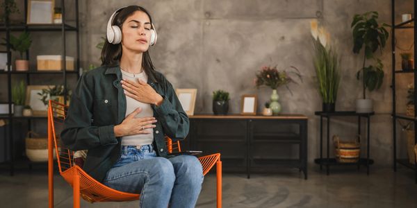 Young woman meditating with headphones on in a cozy room.