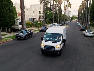 White delivery van driving down a palm tree-lined street in a residential area.
