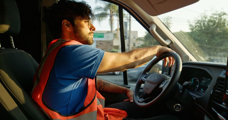 A young, Indian delivery person driving his van during a shift at sunset in Los Angeles, California.