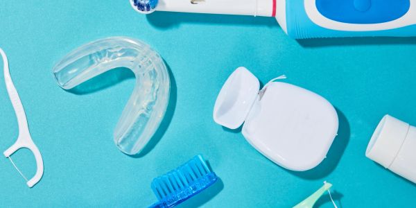Various dental products laying on a blue screen floss, toothbrush, nightguard, toothpaste floss pick