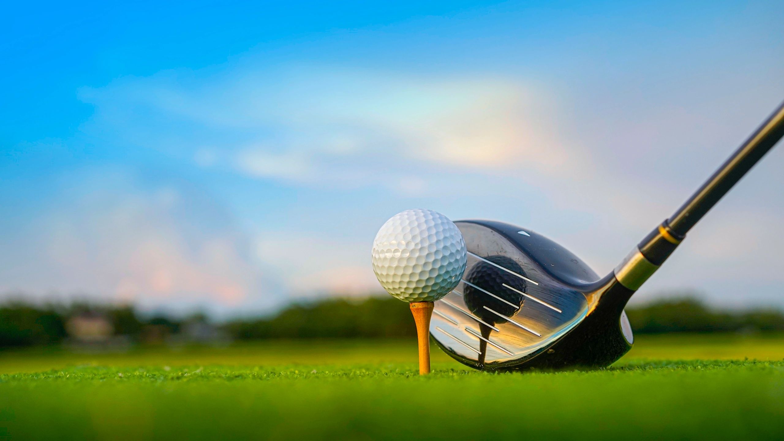 Golf ball on tee with club ready to hit.
