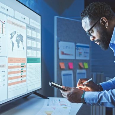 Man analyzing data on a tablet with charts and graphs on a large screen.