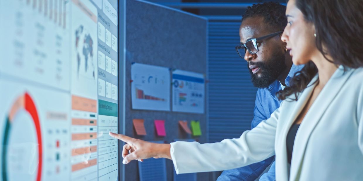 Two professionals analyzing data on a large digital screen in an office.