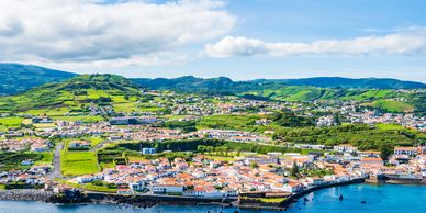 Scenic coastal town with green hills and blue waters under a partly cloudy sky.