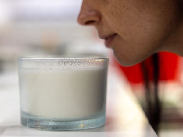 Person smelling a scented candle in a glass container.