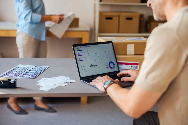 A closeup of a business team in a warehouse using a laptop to analyze shipping data and package orders.