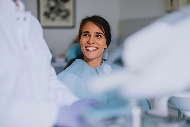Smiling woman sitting in a dental chair interacting with a dentist during a checkup. Dentistry, healthcare, and patient care concepts.