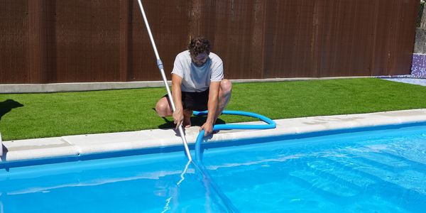 Man cleaning a pool with a vacuum hose on a sunny day.