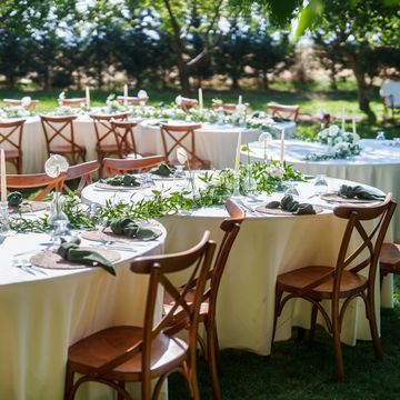 Elegant outdoor wedding tables set with greenery and wooden chairs.