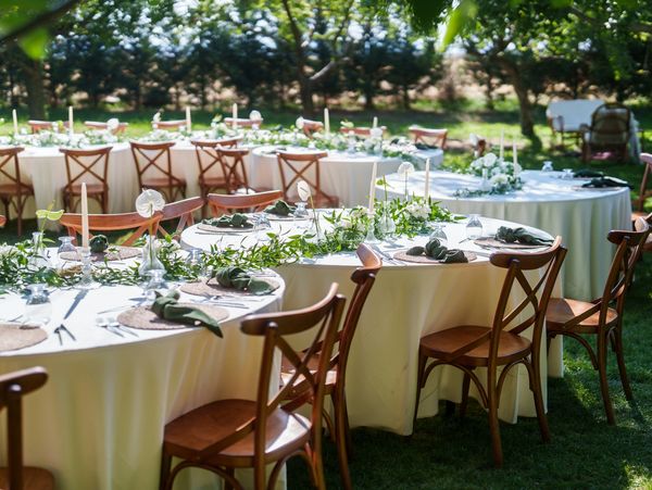 Elegant outdoor tables set for a garden event with wooden chairs and floral centerpieces.