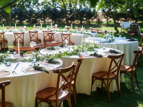 Elegant outdoor tables set for an event with white tablecloths and wooden chairs.