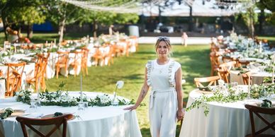 Woman standing at a beautifully decorated outdoor event with tables and string lights.
