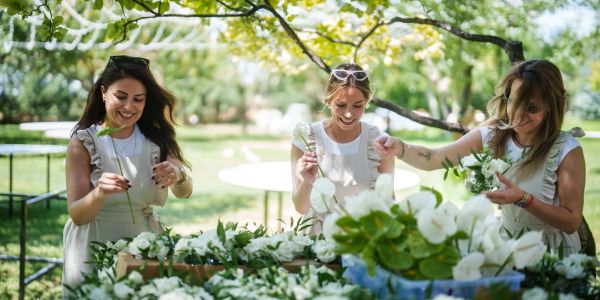 Three women arranging flowers outdoors on a sunny day.