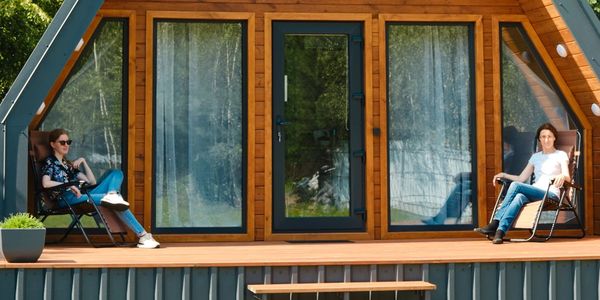 Two women relaxing on chairs outside a wooden cabin.