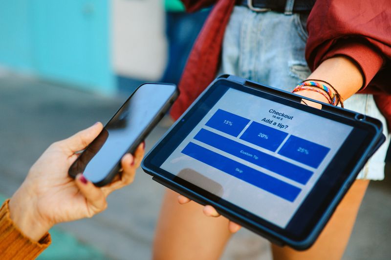 Woman in her 40s woman uses digital tablet to pay and tip the barista in Santa Monica, California. Smart phone tech and contactless payment concepts.