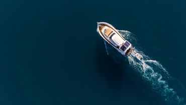 Aerial view of a white boat with solar panels cruising on deep blue water.