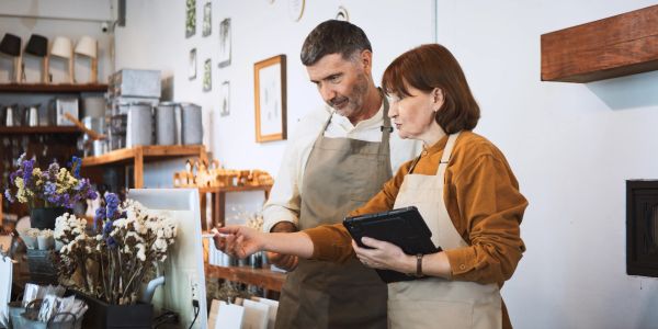 Two people in aprons discussing something on a tablet and computer.