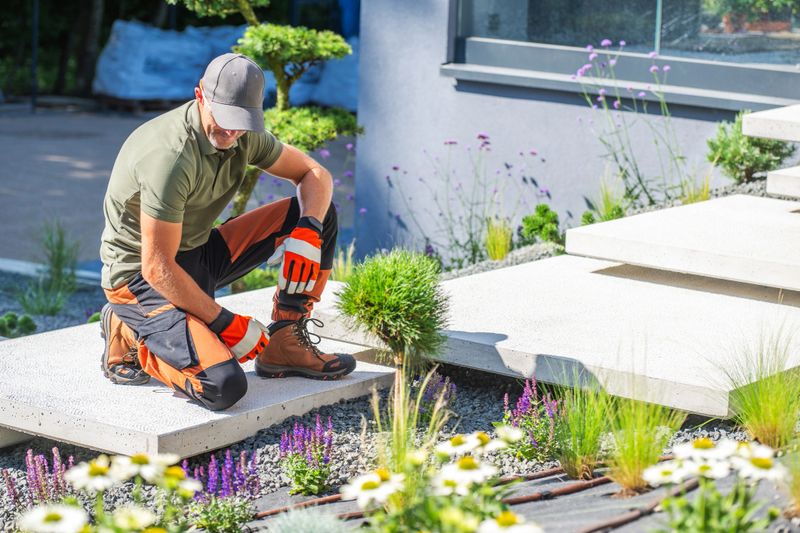 A gardener kneels on a path, planting flowers among decorative stones and greenery in a contemporary garden.