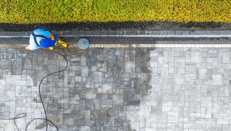 A worker uses a pressure washer to clean a stone patio, revealing a fresh and tidy surface in a well-maintained outdoor area.