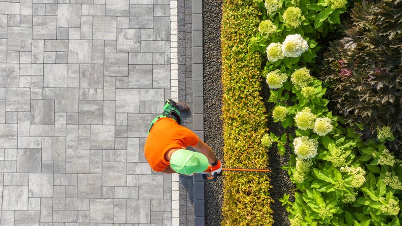 A gardener in bright attire trims hedges in a beautifully landscaped garden filled with blooming flowers.