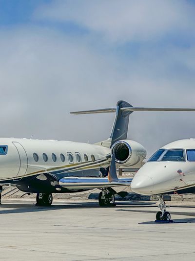 Two private jets parked on a tarmac under a partly cloudy sky.