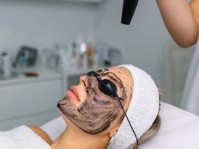 Woman receiving a facial treatment with a carbon mask and protective goggles.