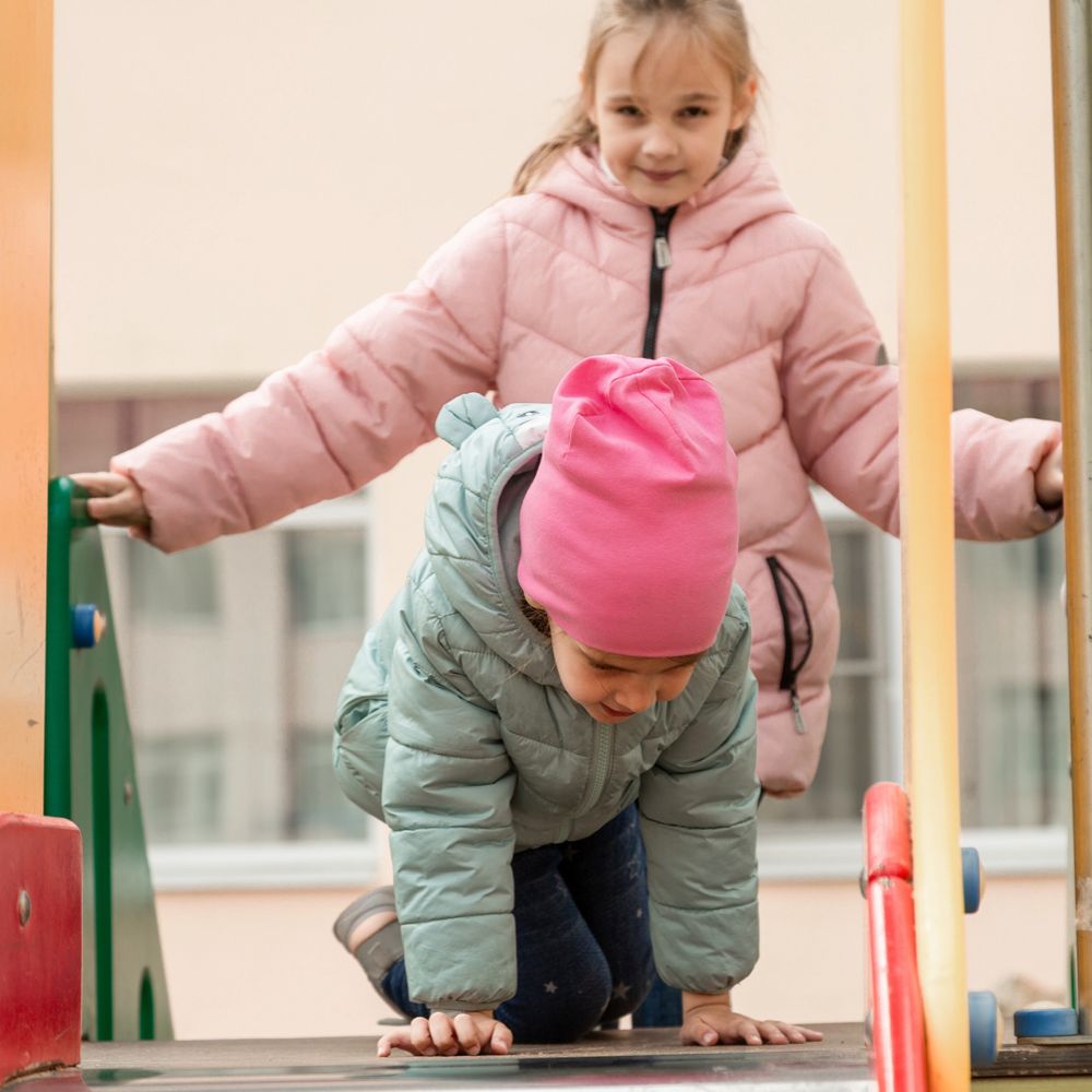 Two children playing on playground equipment in winter jackets.